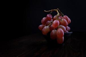 grappe de raisins rouges mûrs dans une assiette en argile. beaux raisins sur fond sombre. photo