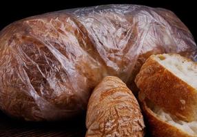 une miche de pain enveloppée dans un sac plastique et des tranches de pain de mie à proximité. photo