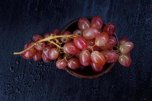 une grappe de raisins rouges mûrs dans une plaque d'argile, sur fond noir avec des gouttes d'eau. vue d'en-haut . photo