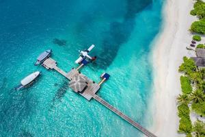 vue aérienne du bungalow sur pilotis et du fond bleu de la mer aux maldives. hydravion et bateaux dhoni en bois sur le lagon tropical. paysage aérien, voyage exotique et concept de vacances. vue de drone sur la scène de la plage photo