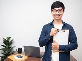 portrait jeune homme d'affaires tenir le tableau des documents debout smlie dans sa salle de travail photo