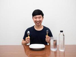 homme joyeux sourire heureux s'asseoir à table tenant des couverts prêts à dîner avec de l'eau sur la table photo