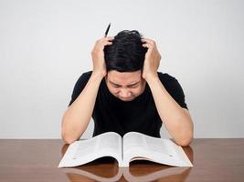 un homme asiatique a mal à la tête en lisant un livre sur la table photo