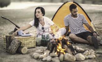 concept de vacances de pique-nique. beau couple s'amusant à faire un barbecue sur un feu de joie et à se détendre au bord d'un lac. photo