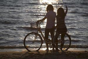 vélo de silhouette et couple amoureux pendant les vacances à l'heure du lever du soleil au bord d'un lac photo