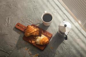 petit déjeuner avec croissant sur planche à découper et café noir. concept de repas du matin et de petit-déjeuner. photo