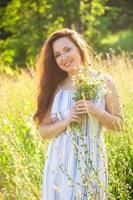 jeune femme marchant parmi les fleurs sauvages le jour d'été ensoleillé. concept de la joie de communiquer avec la nature estivale photo