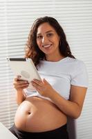 femme enceinte hispanique utilisant une tablette numérique pendant le petit-déjeuner. technologie, grossesse et congé de maternité photo