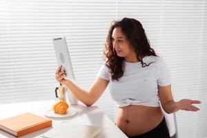 heureuse jeune femme enceinte belle parler à maman en utilisant l'appel vidéo pendant le petit déjeuner du matin. concept de communication et d'attitude positive pendant la grossesse photo