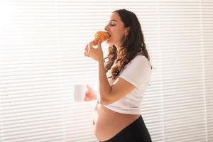 femme enceinte mangeant un croissant et boit du café. grossesse et congé de maternité photo