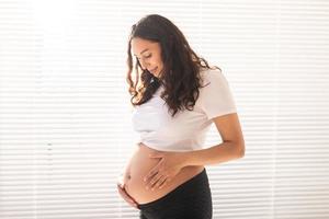 souriante jeune belle femme enceinte touchant son ventre et se réjouissant. concept de sentiments positifs et agréables en attendant le bébé photo