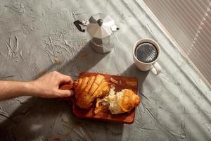 petit déjeuner avec croissant sur planche à découper et café noir. concept de repas du matin et de petit-déjeuner. photo