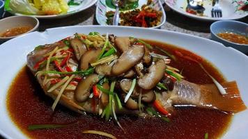 gros plan de bar cuit à la vapeur avec de la sauce soja et des légumes frais, des champignons tranchés, du gingembre, du piment rouge et de l'oignon de printemps sur une assiette blanche ou un plat de style chianese. photo