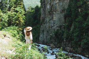 jeune femme voyageuse aux longs cheveux blonds en chapeau de paille regarde la belle vue sur la rivière de montagne, les gens de derrière photo