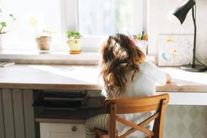 petit enfant belle fille aux cheveux longs dans des vêtements de maison peinture au bureau dans la chambre des enfants à la maison photo