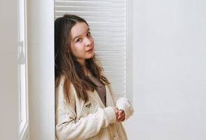 portrait d'une belle adolescente aux longs cheveux noirs près de la fenêtre sur fond blanc photo