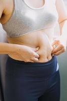 belle grosse femme avec ruban à mesurer, elle utilise sa main pour presser l'excès de graisse isolé sur fond blanc. elle veut perdre du poids, le concept de chirurgie et décomposer les graisses sous le photo