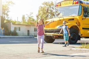 belle petite écolière avec ses camarades de classe près du bus scolaire photo