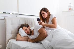 la femme regarde secrètement le téléphone du mari pendant que le mari dort. la femme espionne le téléphone de son mari pendant qu'il dort. le concept de méfiance, de trahison, de jalousie, de relations, de problèmes. photo