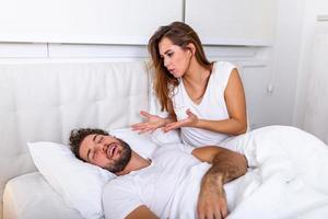 couple au lit, l'homme ronfle et la femme ne peut pas dormir. ronflement homme et jeune femme. couple dormant dans son lit. la jeune fille ne peut pas dormir à cause du ronflement de son homme qui se tient le nez. problème d'homme qui ronfle photo