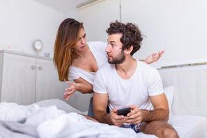 je ne supporte pas quand il travaille tout le temps. jeune femme malheureuse et son petit ami qui utilise le téléphone au lit. conflit familial avec femme mari au lit photo