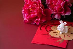 nouvel an chinois du concept du festival du lapin. mandarine, enveloppes rouges, lapin et lingot d'or à décor de fleur de prunier sur fond rouge. photo