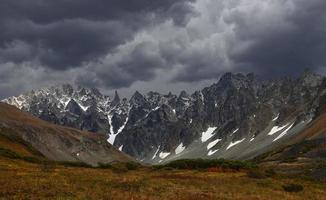 des nuages orageux bas touchent le sommet de la montagne enneigée. paysage impressionnant couvert lugubre avec de gros rochers et glacier photo