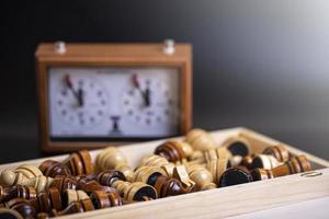 pièces d'échecs sur un plateau et une horloge d'échecs sur fond sombre photo