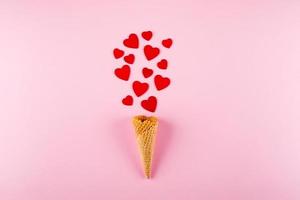 cornet de crème glacée avec des coeurs rouges sur fond rose. amour, concept de la saint-valentin. vue de dessus, mise à plat photo