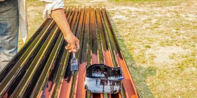 gros plan de la main d'un ouvrier peintre tenant une parcelle de peinture travaillant de la peinture noire sur un tas de tiges de fer. photo