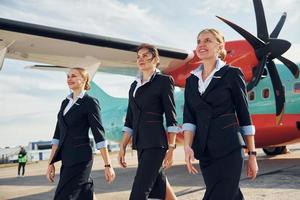 trois hôtesses. équipage de travailleurs de l'aéroport et de l'avion en vêtements formels debout ensemble à l'extérieur photo