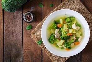 soupe au poulet avec brocoli, pois verts, carottes et céleri dans un bol blanc sur fond bois de style rustique. vue de dessus photo