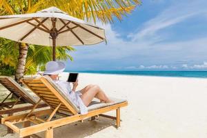 jeune femme au chapeau avec tablet pc à la plage. paysage de plage tranquille parfait, femme détendue travaillant comme bureau à domicile. magnifique paysage naturel sur la plage tropicale. espace de copie pour le texte, été ensoleillé photo