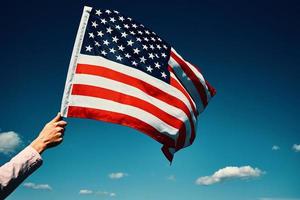 agitant le drapeau américain à la main contre le ciel bleu photo