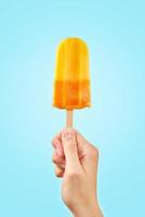 Popsicle de crème glacée aux fruits surgelés jaune à la main sur fond bleu photo