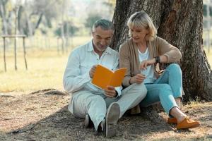 couple de personnes âgées romantique et amoureux lisant un livre sous un arbre dans le parc