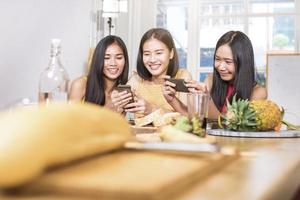 groupe de femmes drôles asiatiques appréciant manger de la nourriture et jouer au téléphone à la maison photo