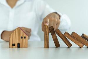 l'assurance avec les mains protège la maison. les mains de l'homme d'affaires empêchent les dominos de tomber dans la crise des affaires. contrôle des risques commerciaux et planification et stratégies pour gérer les entreprises d'assurance. photo