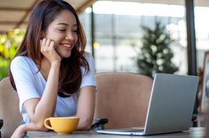 femme asiatique portant un blanc assis dans un café. faites une pause au travail, buvez un café sourire heureux et détendu. photo