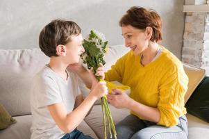 concept de bonne fête des mères ou des femmes. fils enfant félicite sa mère en vacances et donne des fleurs photo