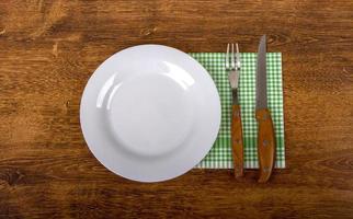 assiette vide, fourchette et couteau sur fond en bois.