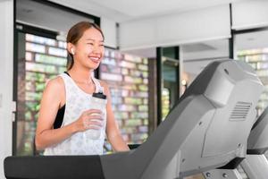 jeune femme asiatique heureuse athlète courir sur tapis roulant, machine à courir, dans une salle de sport intérieure fitness pour la santé photo