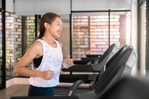 jeune femme asiatique heureuse athlète courir sur tapis roulant, machine à courir, dans une salle de sport intérieure fitness pour la santé photo