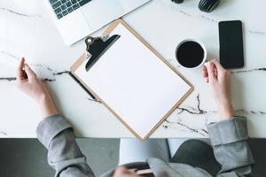 vue de dessus d'une femme d'affaires sur le lieu de travail avec une tasse de café, des notes, un ordinateur portable ouvert, un smartphone sur une table en marbre blanc dans la salle de bureau moderne et lumineuse, une maquette photo