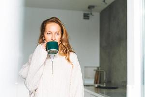 jeune adulte de quarante ans belle femme blonde aux cheveux longs utilisant un smartphone et buvant du thé le matin dans la cuisine à la maison photo
