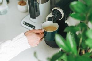 photo de récolte d'une jeune femme verse du café à partir d'une machine à café dans la cuisine à la maison