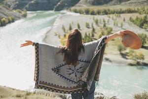 jeune femme brune insouciante voyageur en poncho de dos sur fond magique de rivière de montagne photo