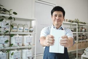 portrait d'un commerçant thaïlandais sourit et regarde la caméra avec un récipient réutilisable, des produits biologiques dans un magasin de recharge, une épicerie zéro déchet et une entreprise durable sans plastique et respectueuse de l'environnement. photo