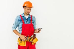 profession, construction et bâtiment - travailleur masculin souriant heureux ou constructeur en casque et dans l'ensemble avec smartphone sur fond blanc photo