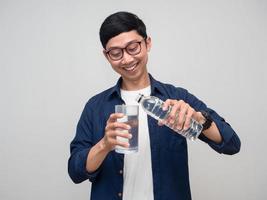 homme positif verser de l'eau dans un verre avec un sourire heureux isolé photo